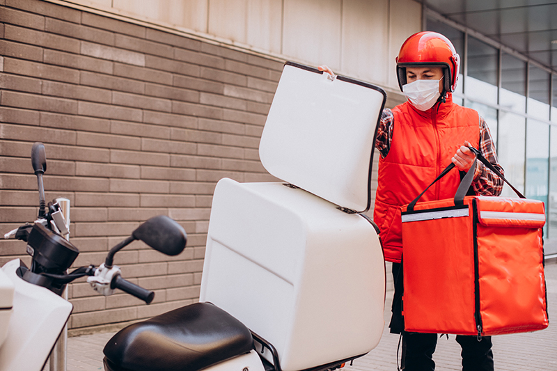 food delivery boy driving scooter with box with food and wearing mask