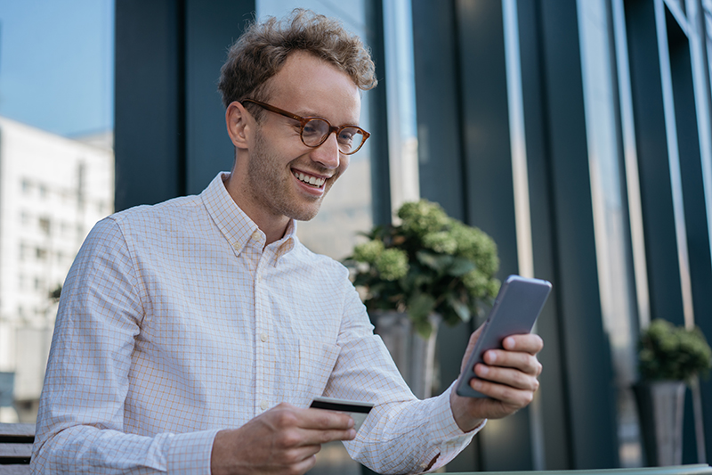 handsome smiling businessman holding credit card using mobile app shopping online